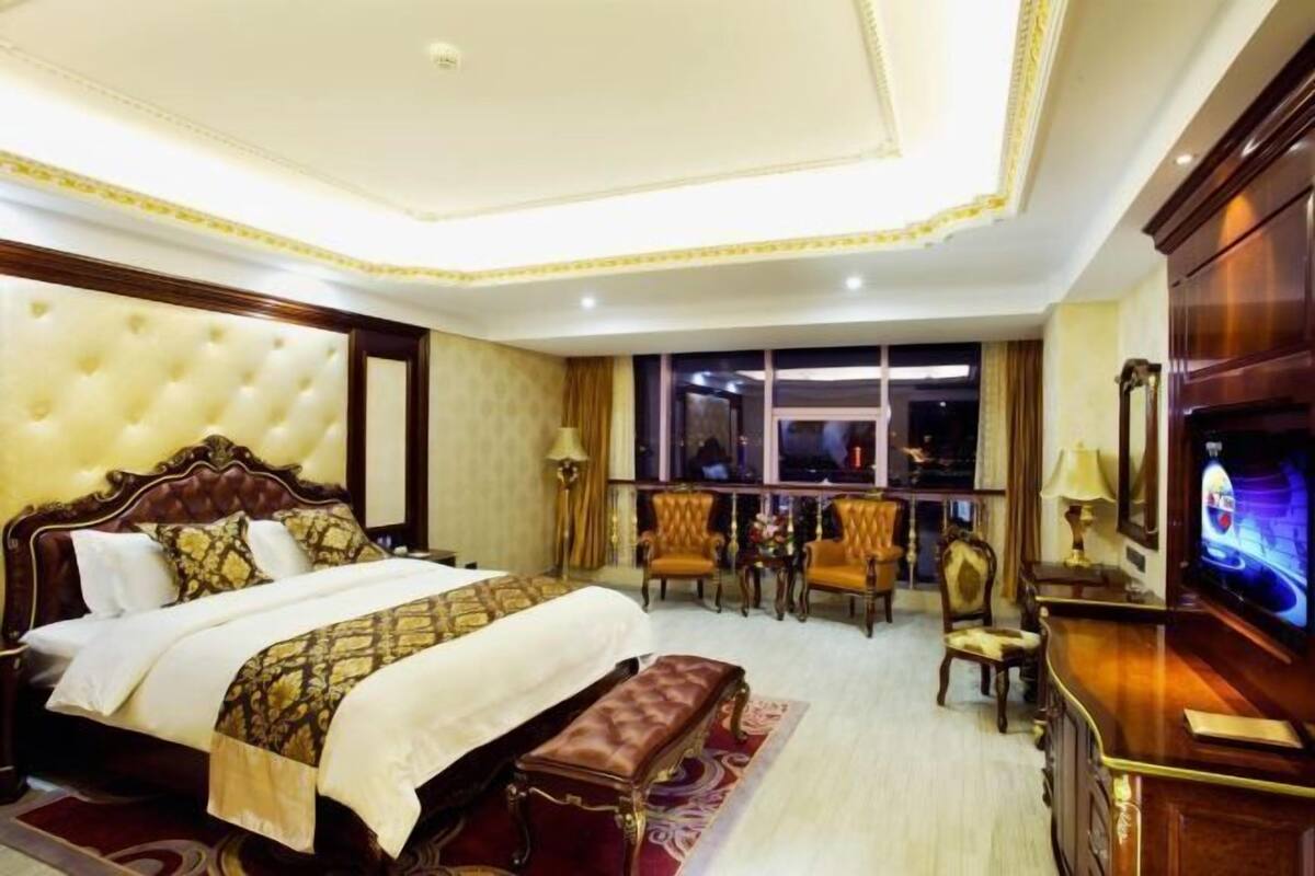 A hotel room with a large bed, a bench, a TV, and a desk with a chair.