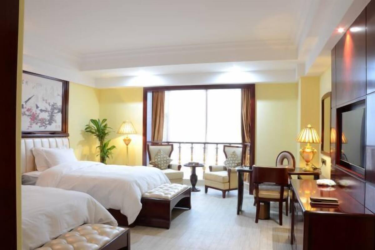 A hotel room with two beds, a dining table, chairs, a TV, and a balcony with curtains.