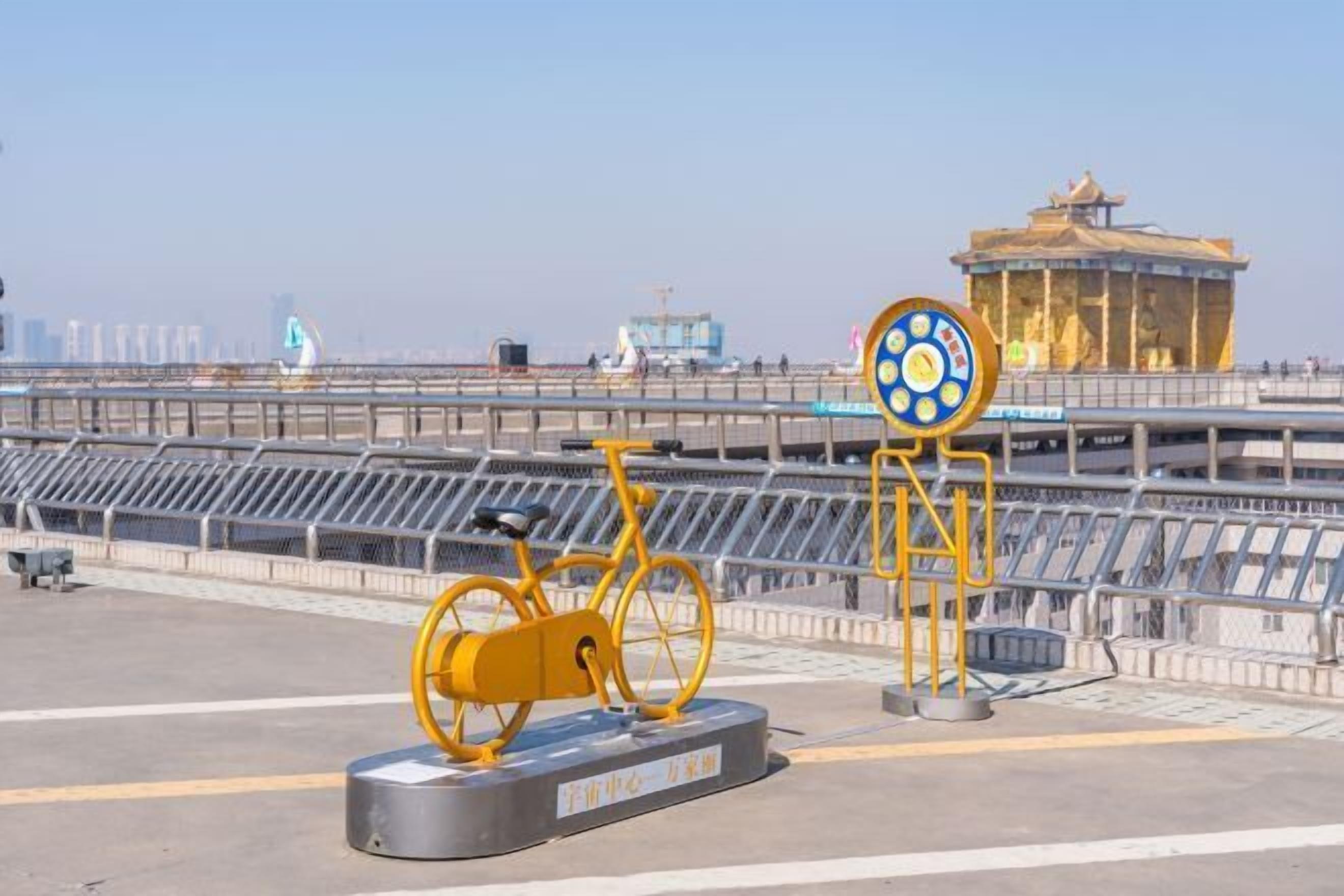 A yellow bicycle sculpture on a platform with a large circular sign in the background.