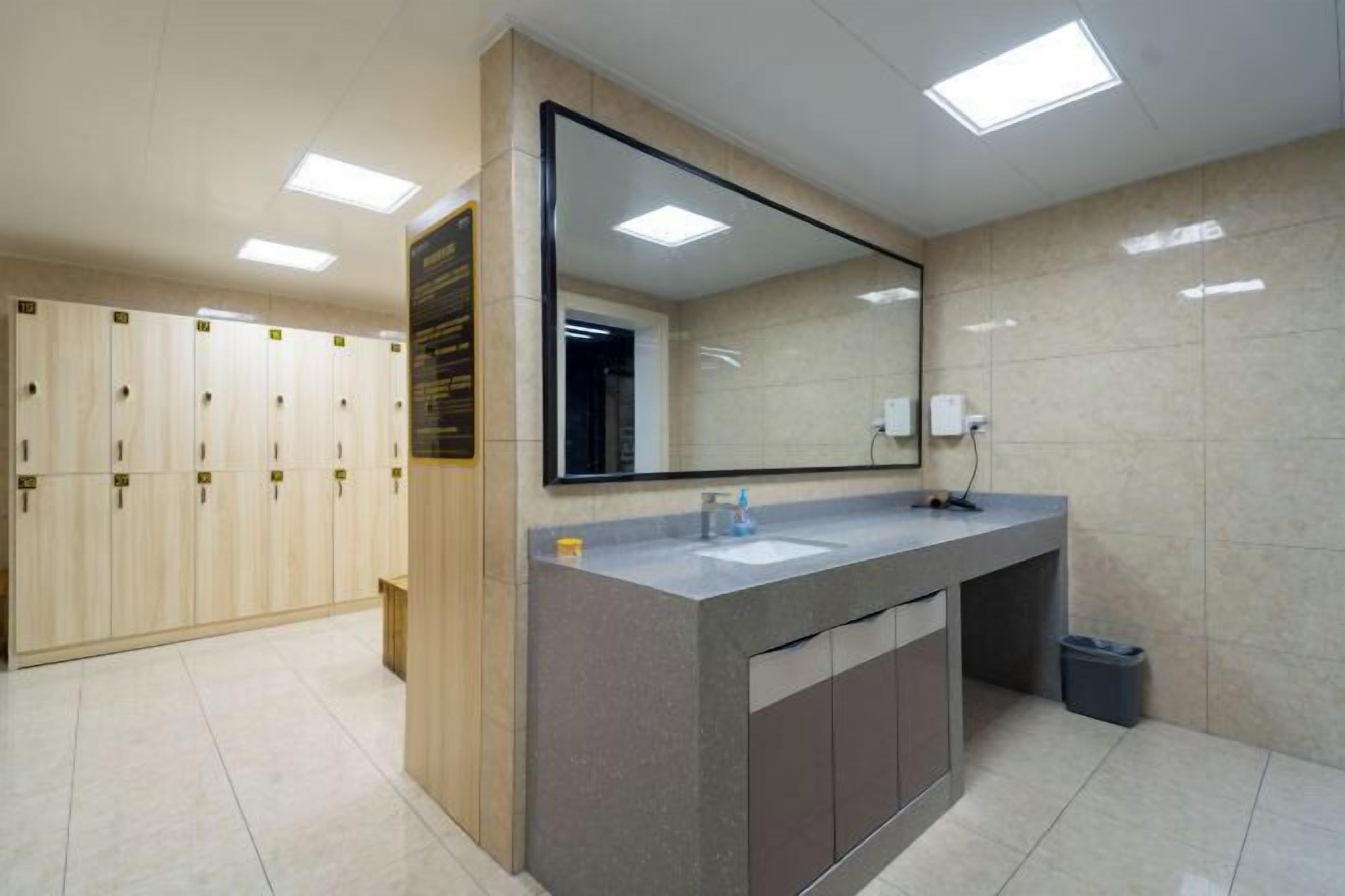 Un baño moderno con un espejo grande, un lavamanos y una fila de taquillas.