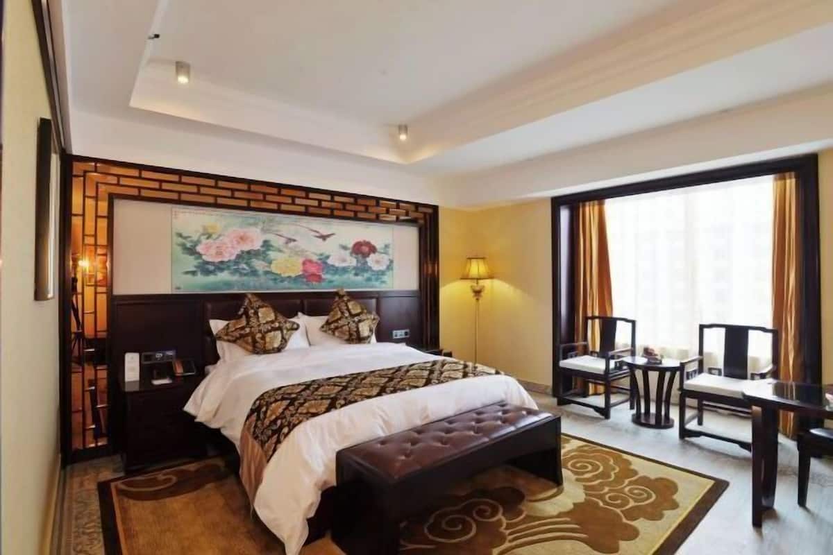 A hotel room with a bed, a desk, a chair, a lamp, and a painting on the wall.