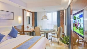 Una habitación de hotel con cama, escritorio, sillas, televisión y un ventanal grande.