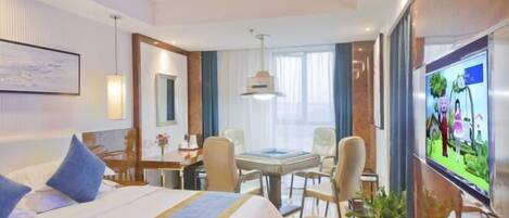 A hotel room with a bed, a desk, chairs, a TV, and a large window.