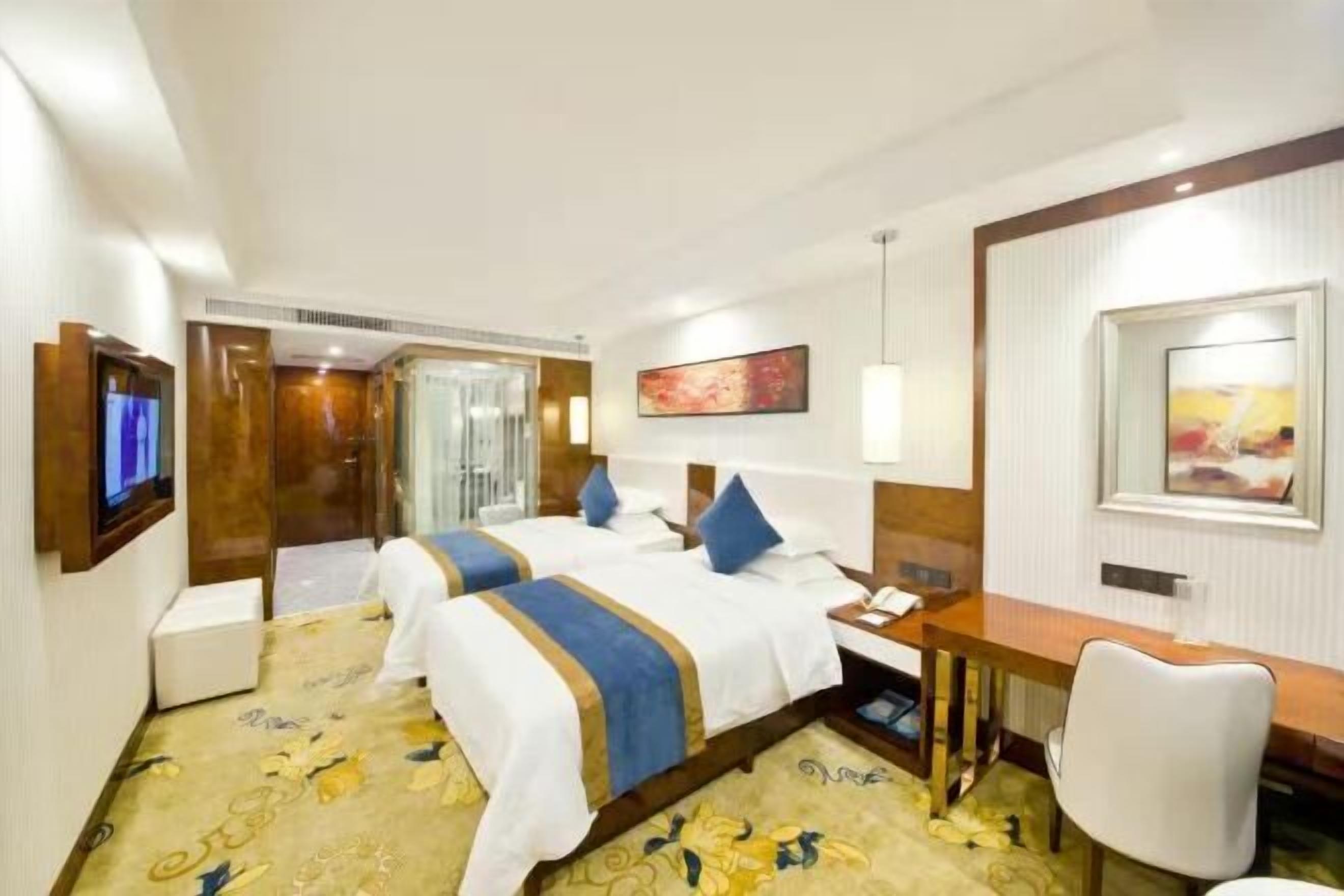 A hotel room with two beds, a desk, a chair, and a TV.