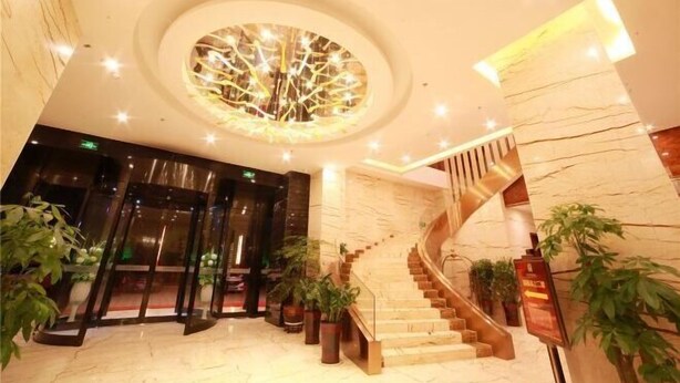 Un vestíbulo de hotel con una lámpara circular en el techo, una escalera y plantas en macetas.