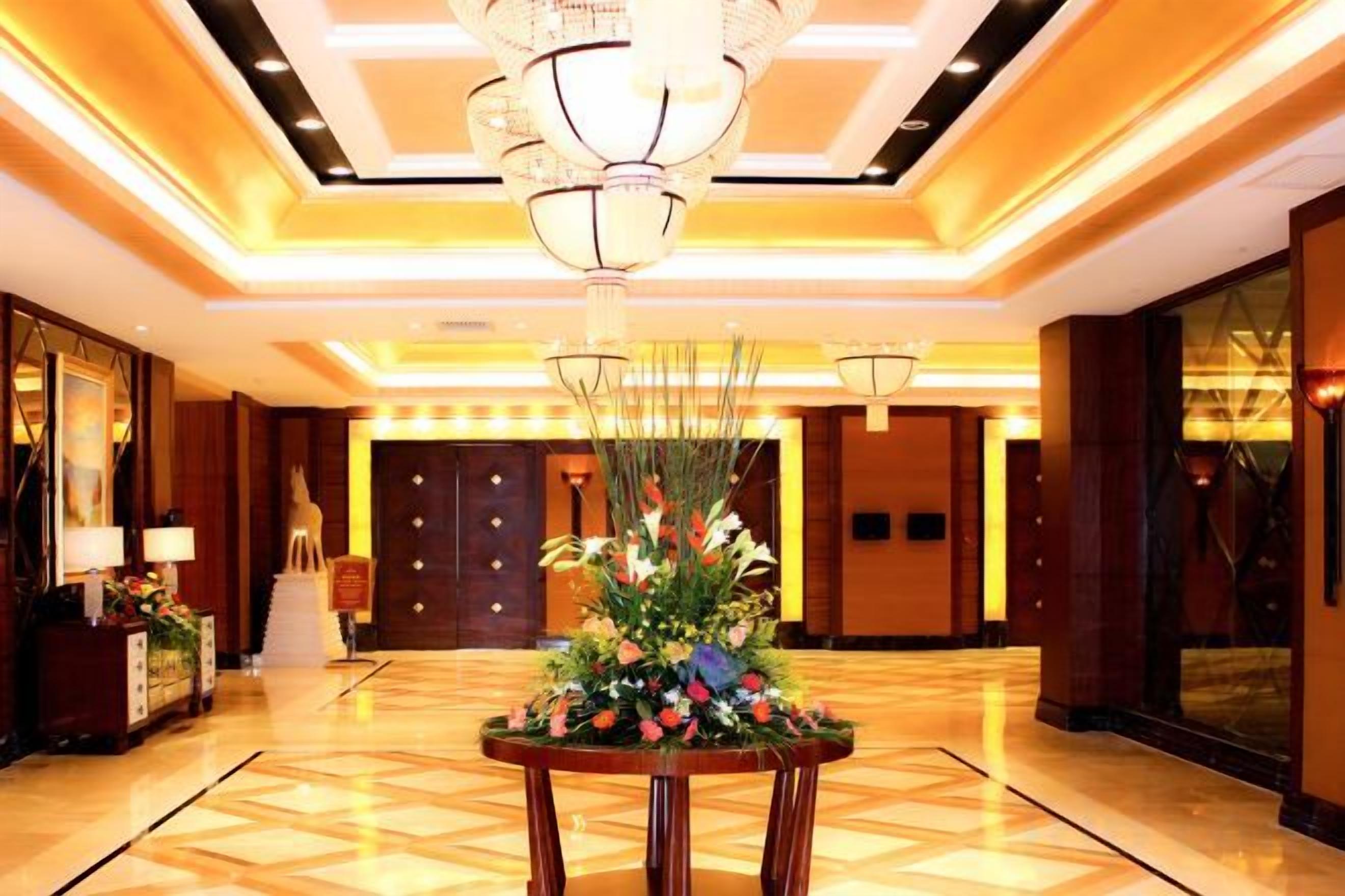 A hotel lobby with a chandelier, a reception desk, and a floral centerpiece.