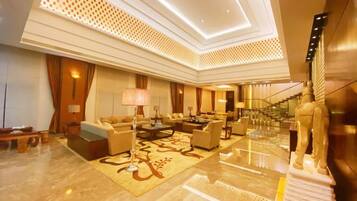 A spacious lobby with a high ceiling, a staircase, and a central seating area with sofas and a coffee table.