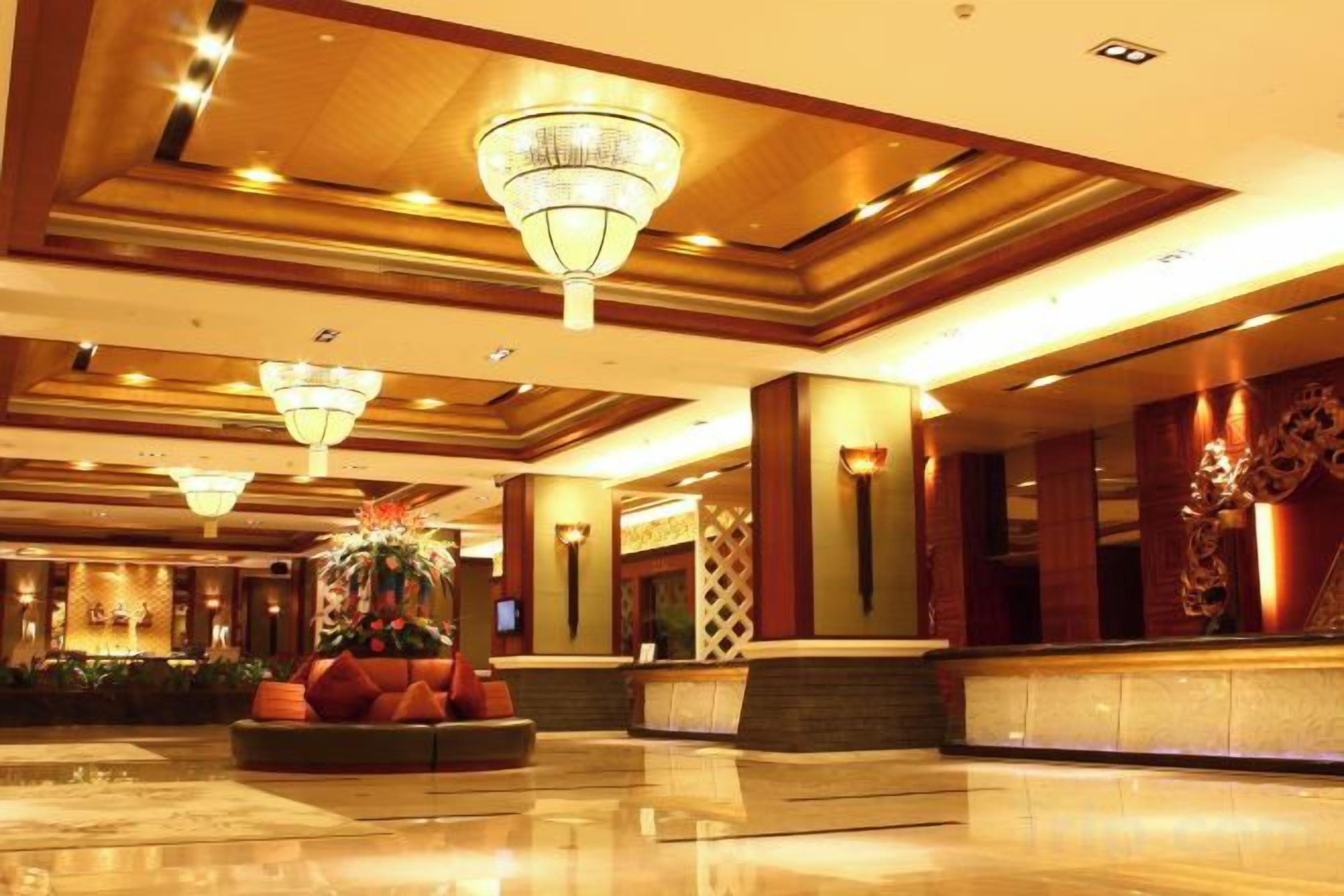 Un vestíbulo de hotel con mostrador de recepción, candelabros y un arreglo floral decorativo.