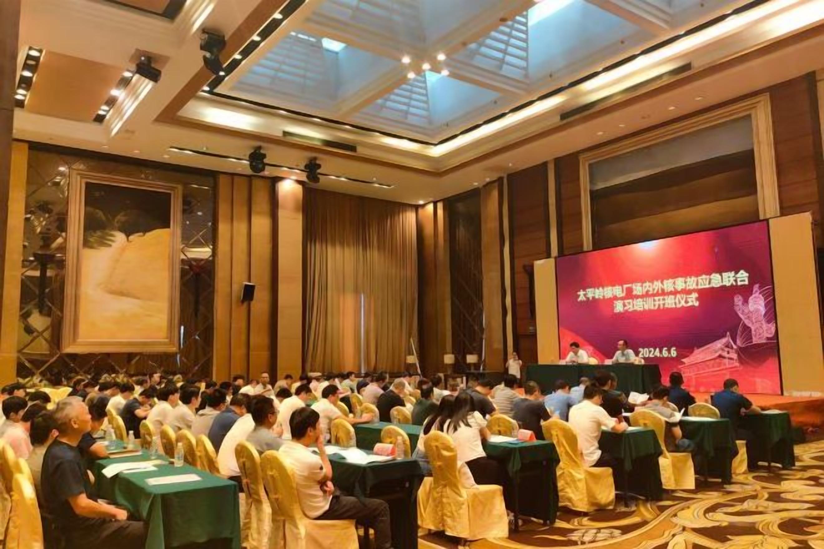 A conference room with rows of tables and chairs, a large screen at the front, and a high ceiling with skylights.