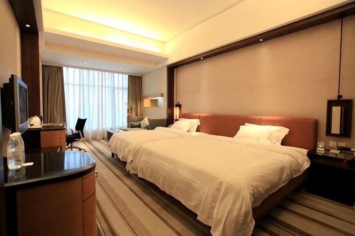 A hotel room with two beds, a desk, a TV, and a large window.