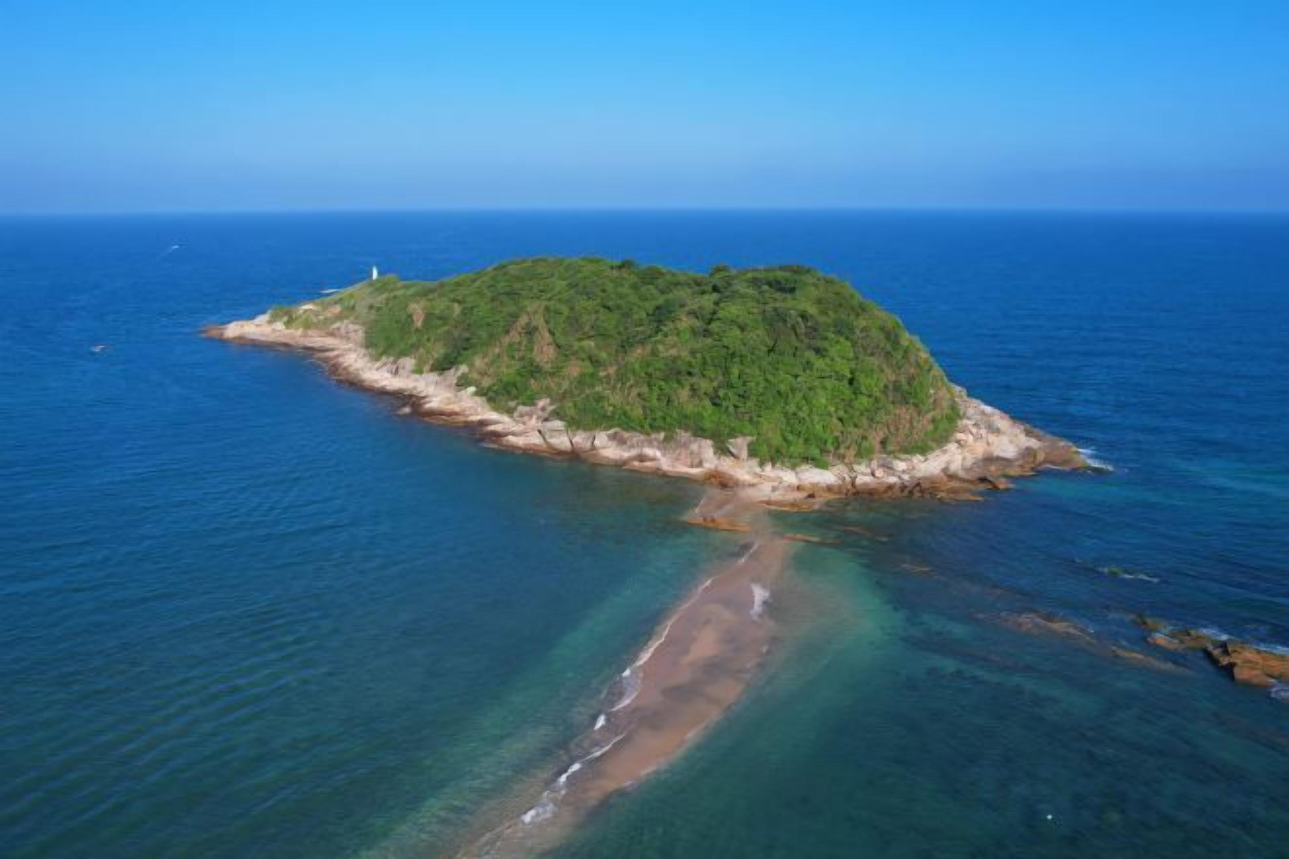 An aerial view of a small island with a beach and clear blue waters.