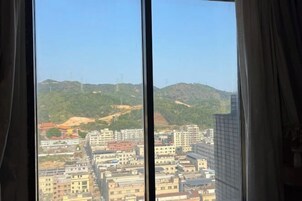 Vista pela janela de um horizonte urbano com edifícios e uma colina ao fundo.