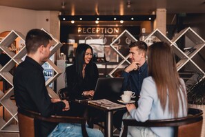 A group of people seated at a table in a cafe with a reception area in the background.