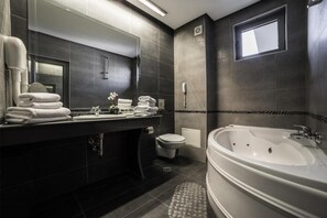 A modern bathroom with a large bathtub, a toilet, and a sink area with towels. - Business Hotel Plovdiv (Plovdiv)