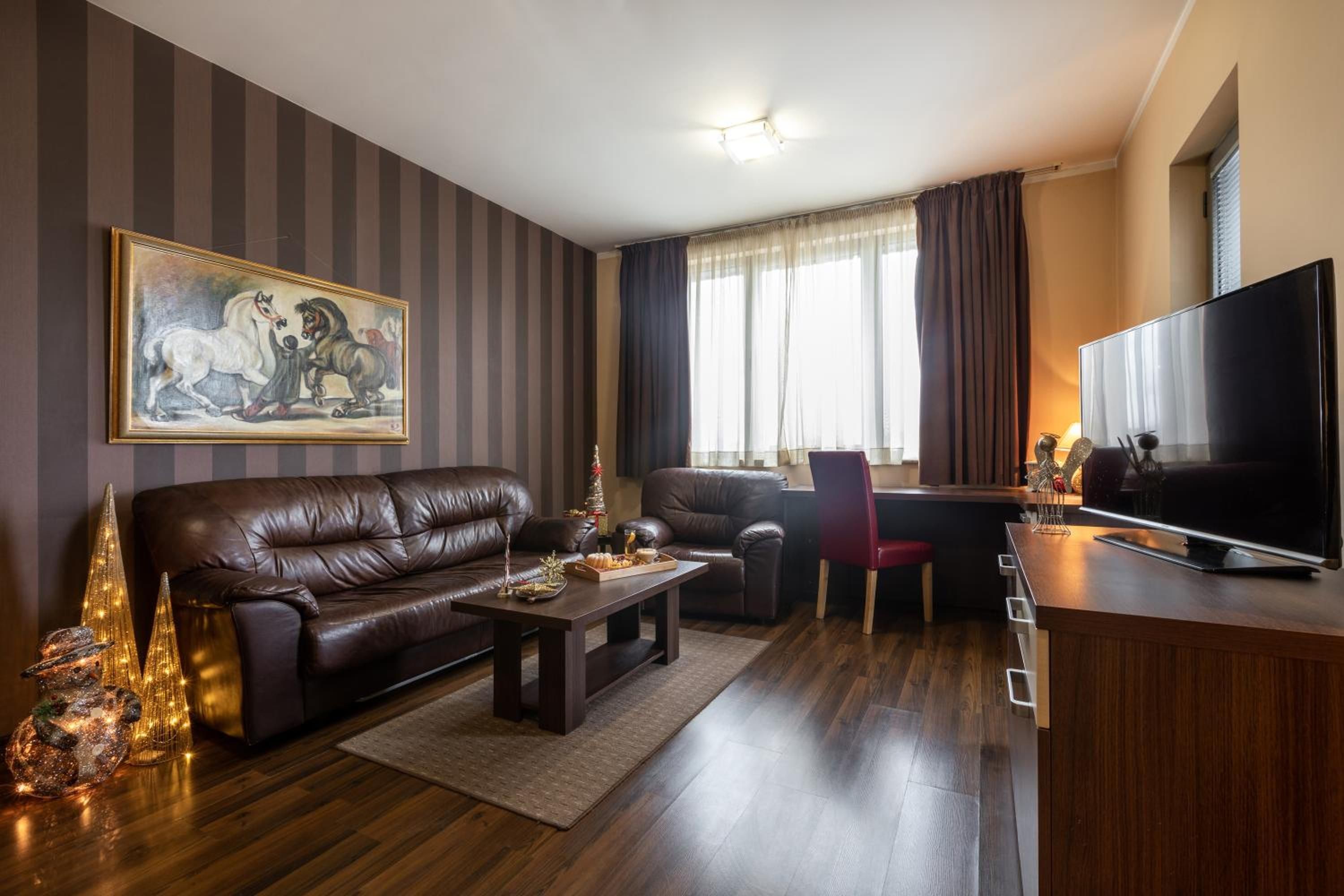 A modern living room with a leather sofa, a dining table, a flat-screen TV, and a painting on the wall.