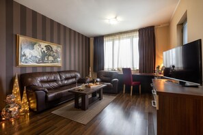 A modern living room with a leather sofa, a dining table, a flat-screen TV, and a painting on the wall.