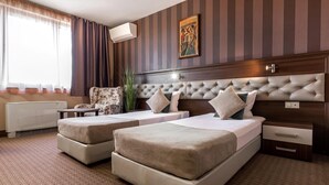 A hotel room with two beds, a bedside table, a radiator, a window with curtains, a painting on the wall, and a plant. - Business Hotel Plovdiv (Plovdiv)
