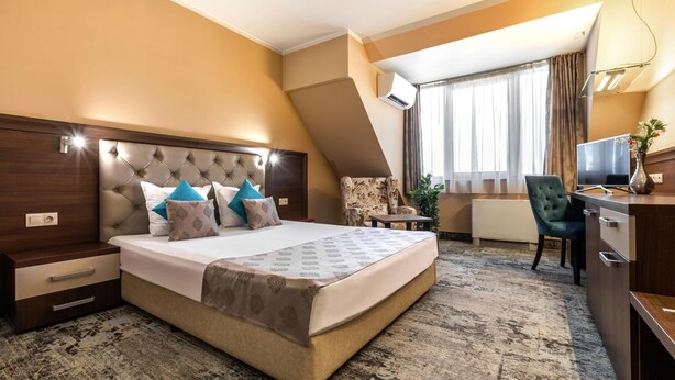 A hotel room with a large bed, a desk, a chair, and a television. - Business Hotel Plovdiv (Plovdiv)