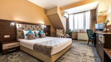 A hotel room with a large bed, a desk, a chair, and a television.