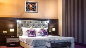 A hotel room with a tufted headboard, a bed with two pillows, a bedside table with a lamp, and a wall-mounted artwork. - Business Hotel Plovdiv (Plovdiv)