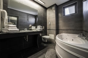 A modern bathroom with a large bathtub, a toilet, and a sink area with towels. - Business Hotel Plovdiv (Plovdiv)