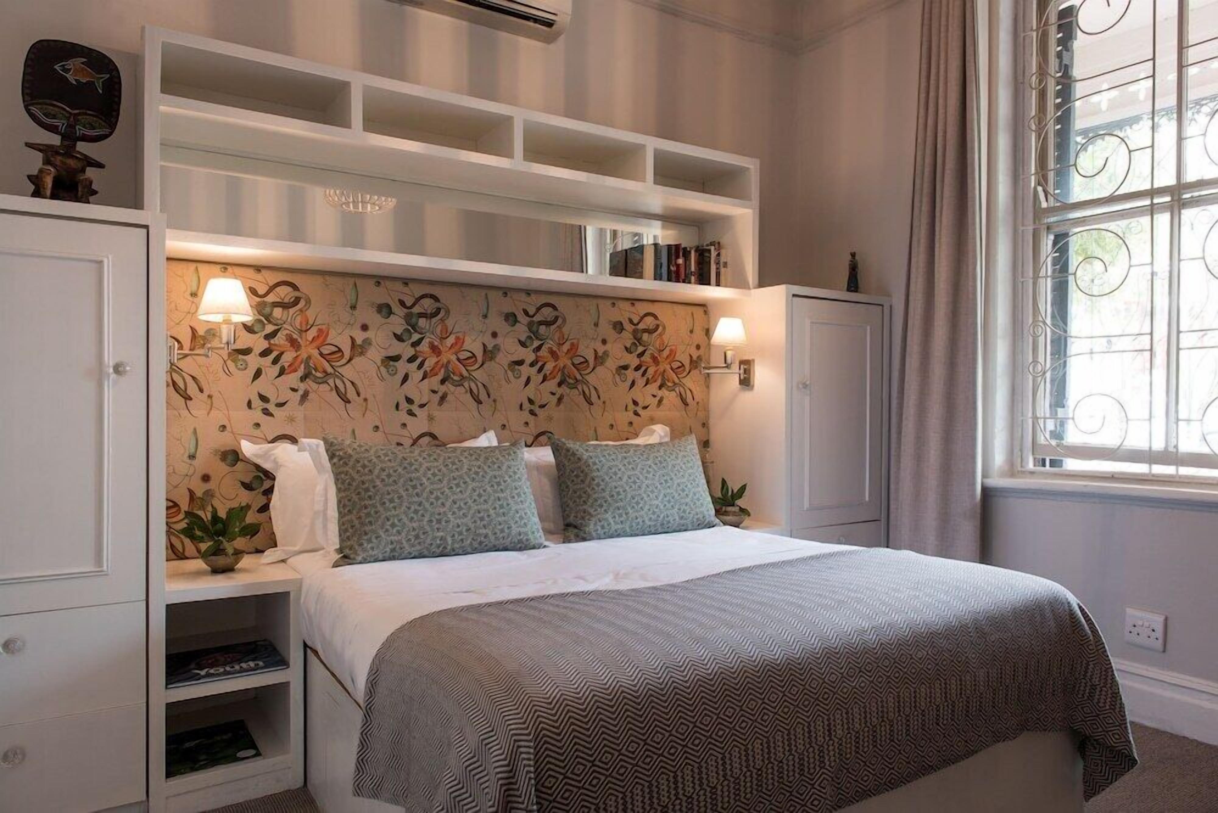 Une chambre à coucher comprenant un lit, des étagères intégrées, une tête de lit décorative et une fenêtre avec des rideaux.