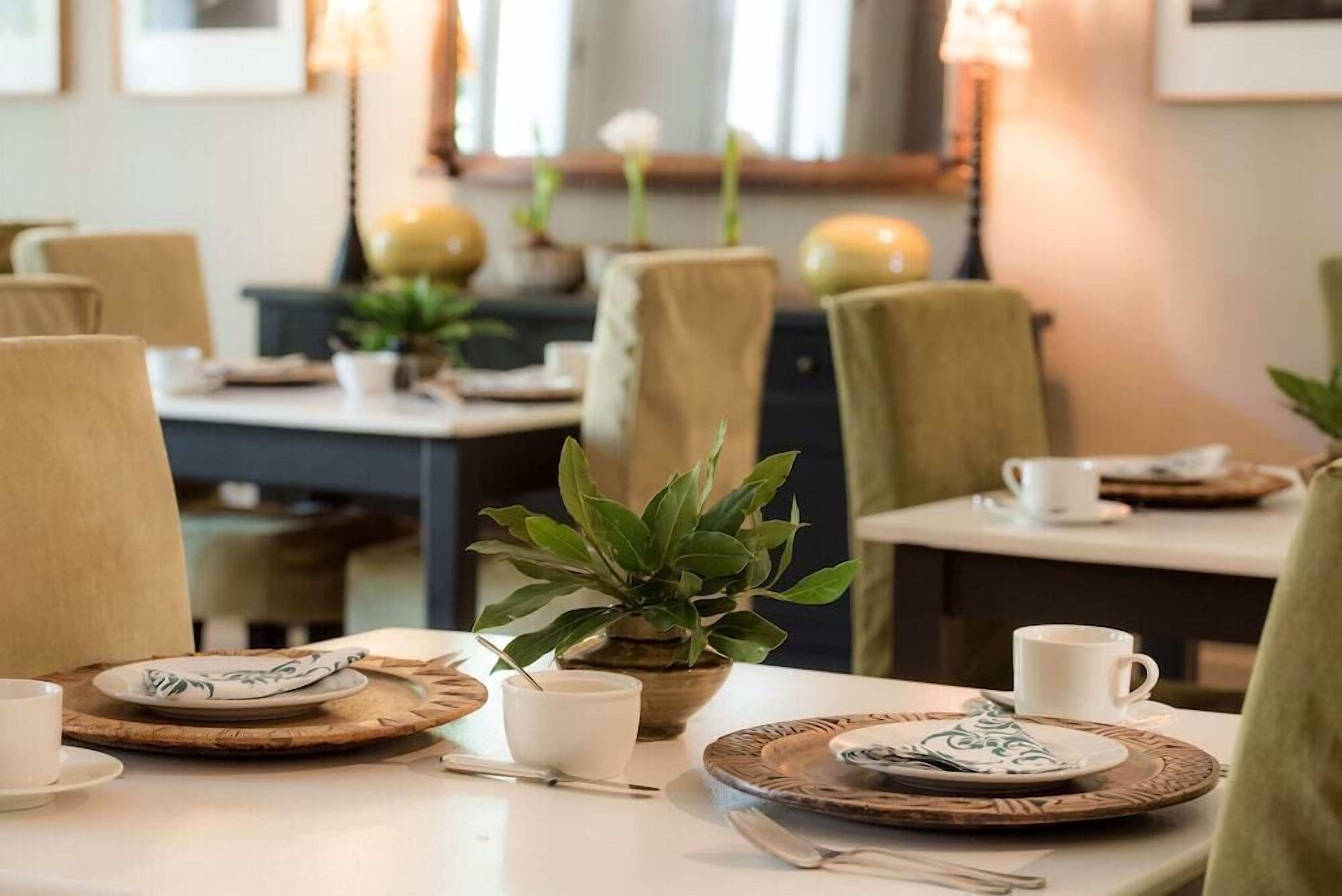 A dining area with tables set for two, featuring woven placemats, white plates, and cups.