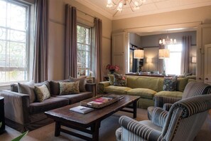 A cozy living room with a brown leather sofa, a green sofa, and a striped armchair. There is a wooden coffee table with a tray of books.
