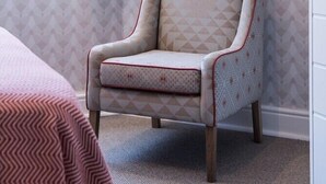 A room with a patterned wallpaper, a chair with a geometric design, and a window with a view of greenery. - Welgelegen Boutique Hotel (Gardens)