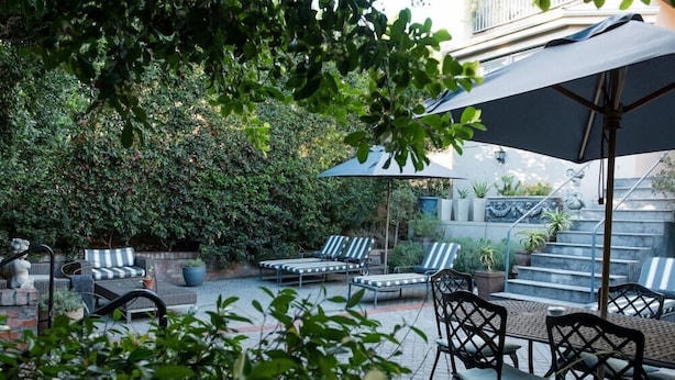 An outdoor patio with lounge chairs and a table, surrounded by greenery and a stone wall. - Welgelegen Boutique Hotel (Gardens)