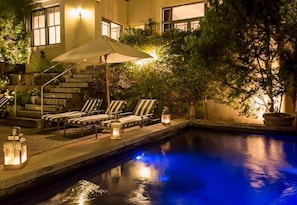 A poolside area with lounge chairs, a staircase, and a well-lit building facade.