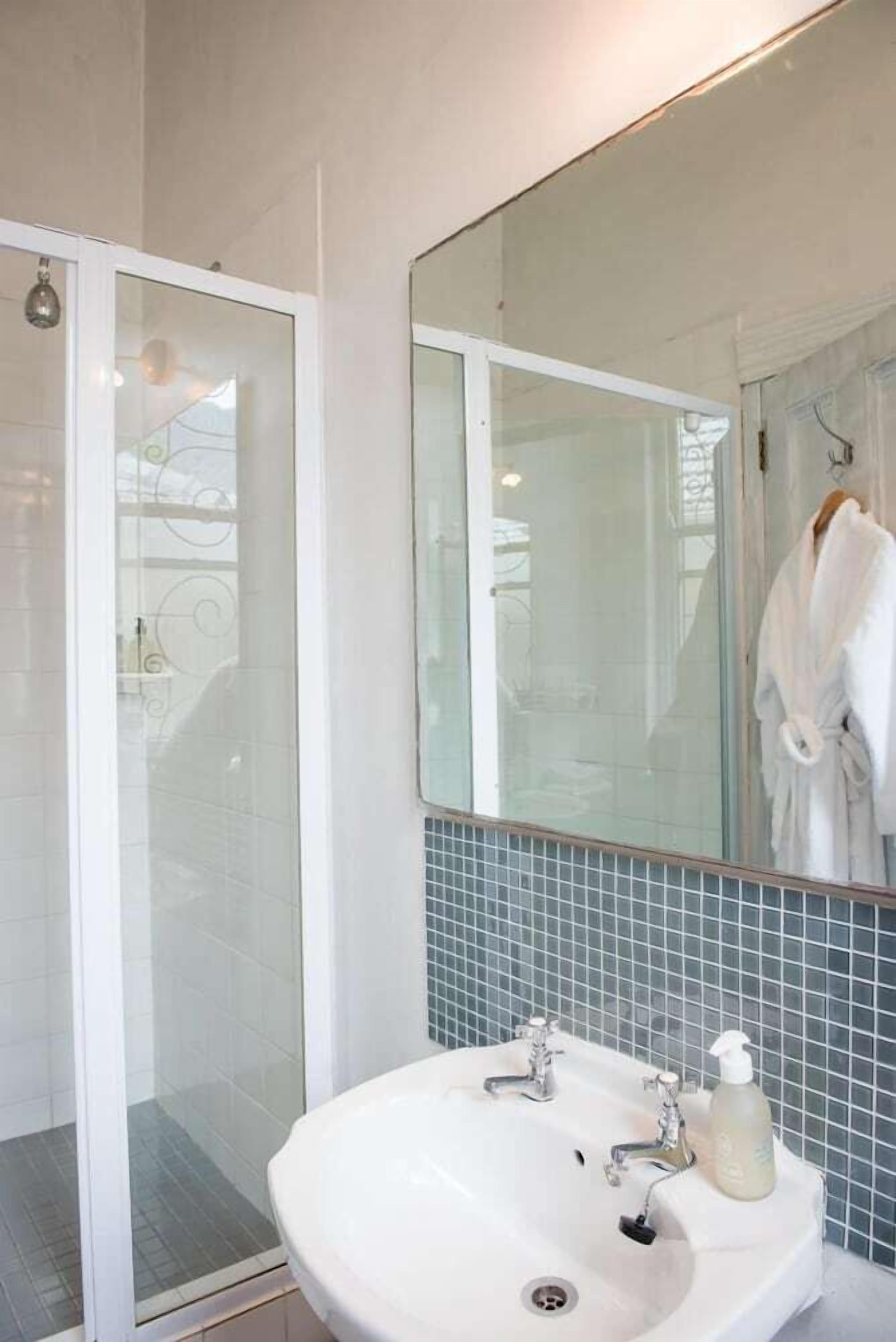 A bathroom with a white sink, two faucets, a mirror, and a glass shower enclosure.