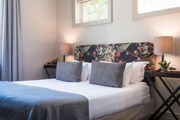 A neatly made bed with patterned bedding, two bedside lamps, and a floral headboard.
