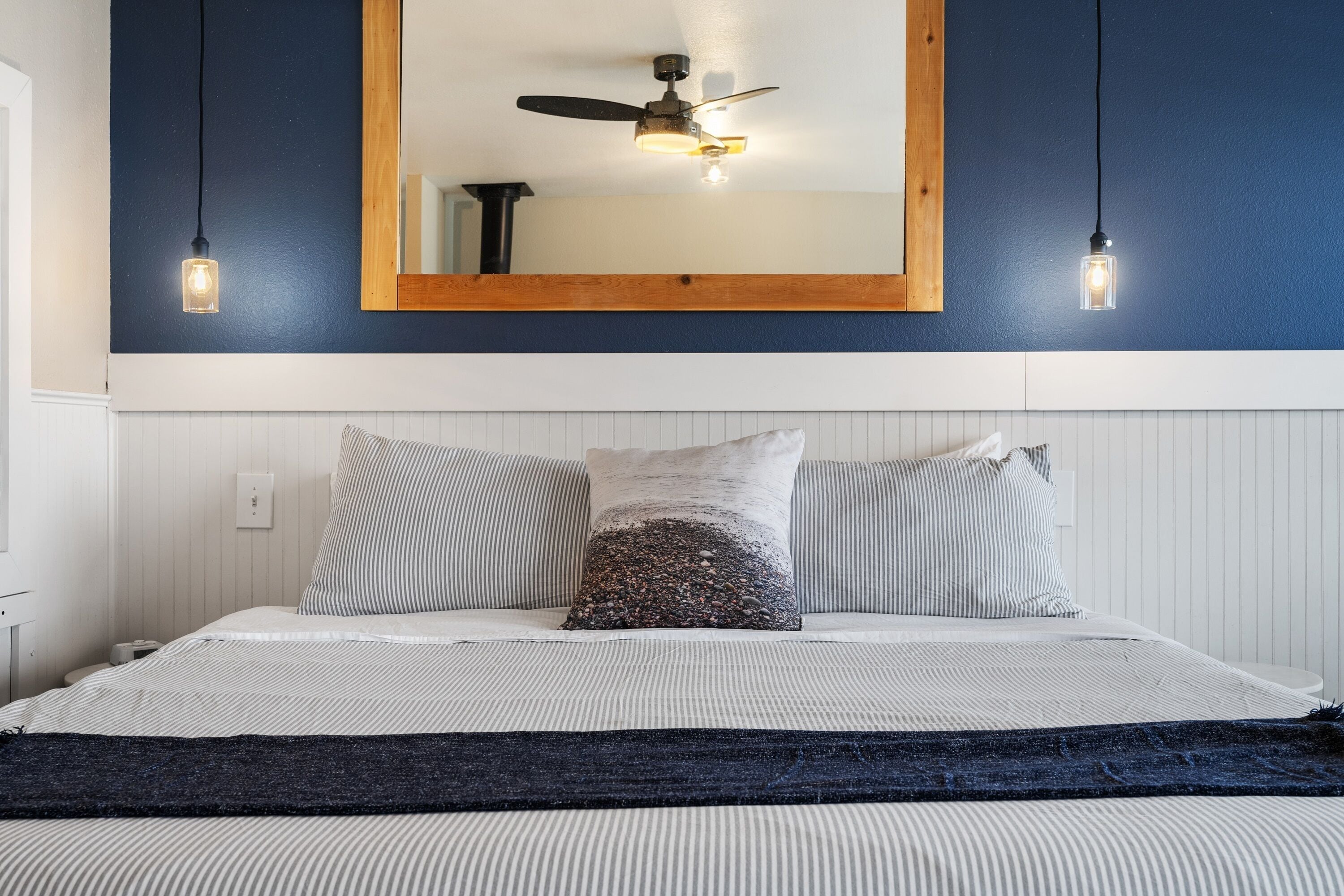 A bedroom with a bed, two bedside lamps, a ceiling fan, and a large mirror above the bed.