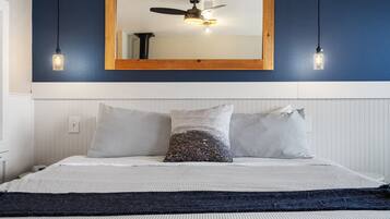 A bedroom with a bed, two bedside lamps, a ceiling fan, and a large mirror above the bed.