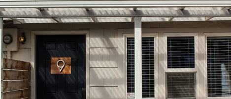 A house with a black door, a number 9 sign, three windows, and a porch with yellow chairs.