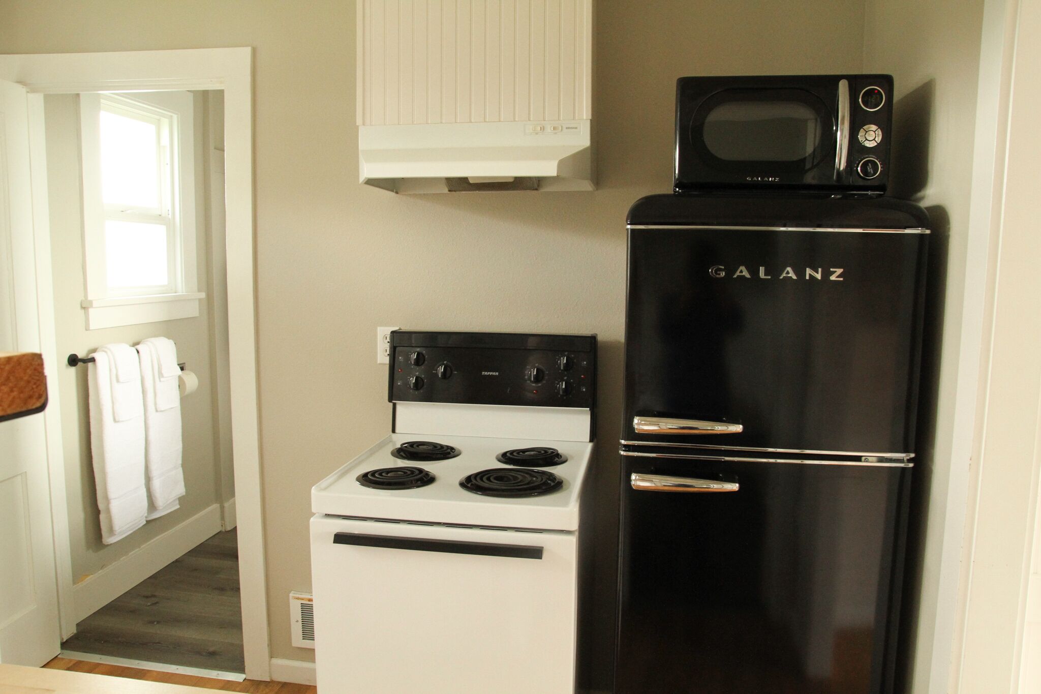 Una cocina compacta con estufa blanca, refrigerador negro y un microondas encima del refrigerador.