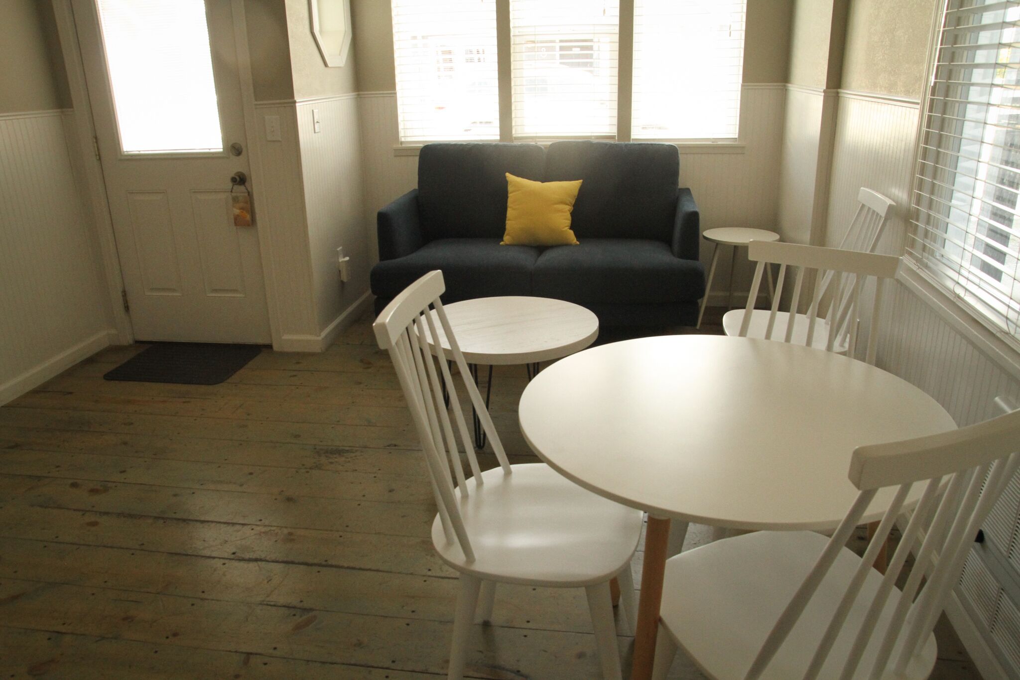 A room with a dark blue sofa, a yellow pillow, a white round table, and white chairs.