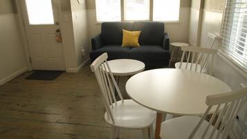 A room with a dark blue sofa, a yellow pillow, a white round table, and white chairs.
