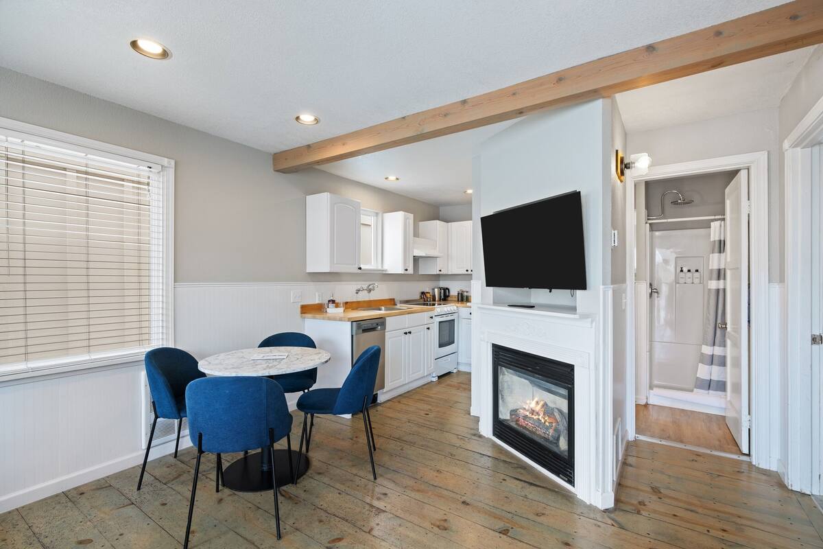 A modern kitchen with white cabinets, a built-in oven, and a TV mounted above the fireplace.