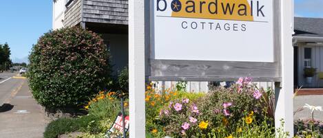 A sign for boardwalk cottages with a clock on the building behind it.