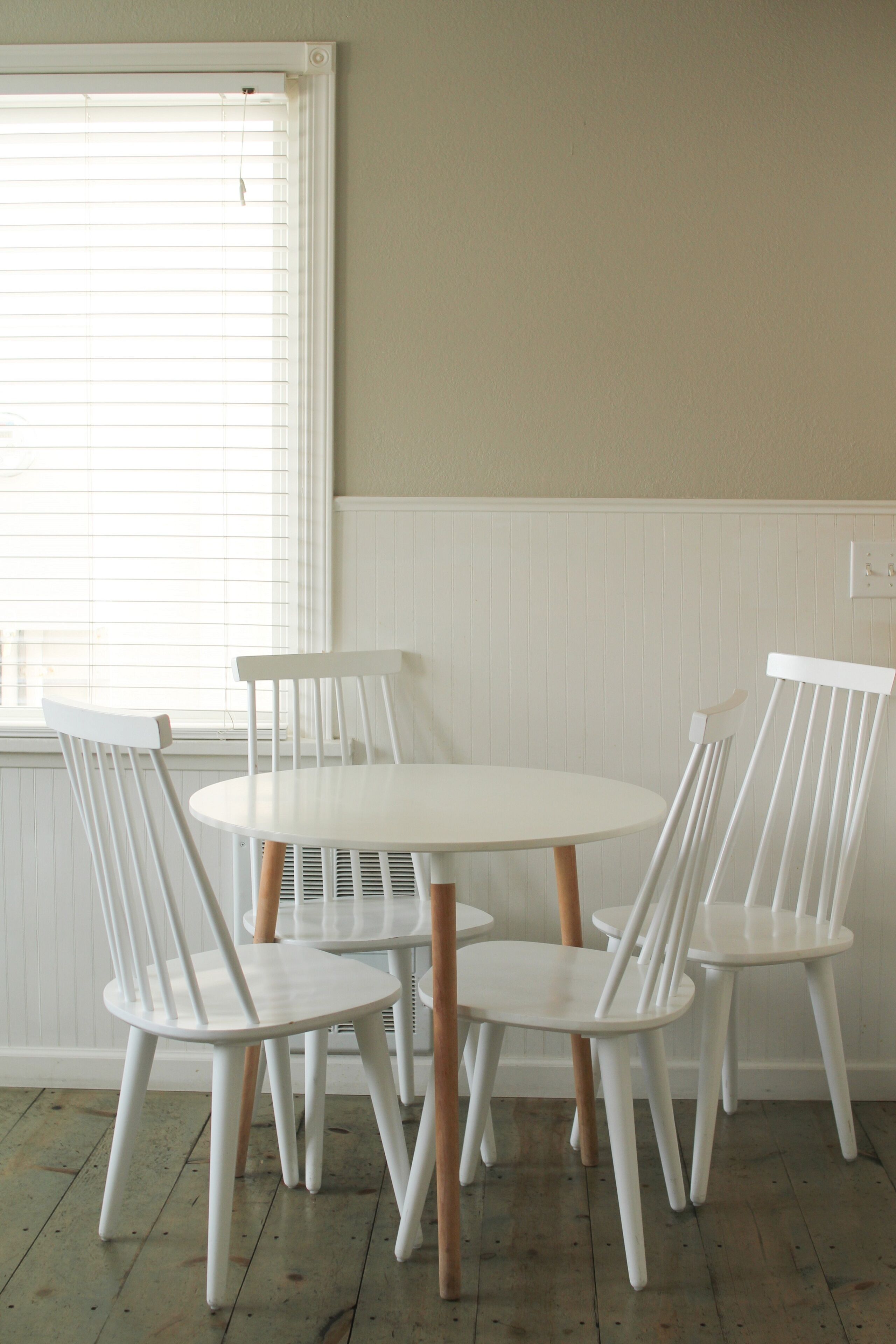 A dining area with a round table and four white chairs with wooden legs.