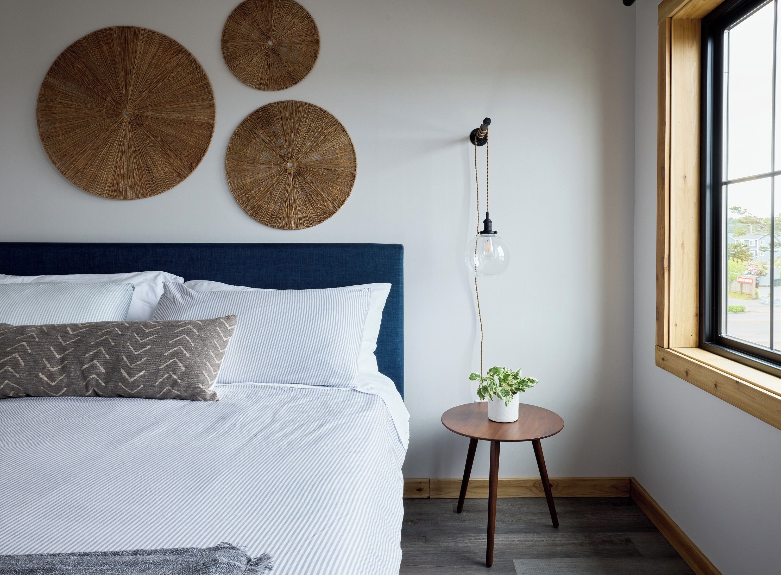 A bedroom with a bed, a round wooden table with a plant, and three round woven wall decorations.
