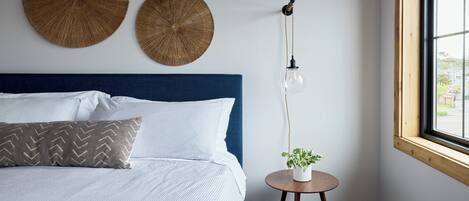 A bedroom with a bed, a round wooden table with a plant, and three round woven wall decorations.