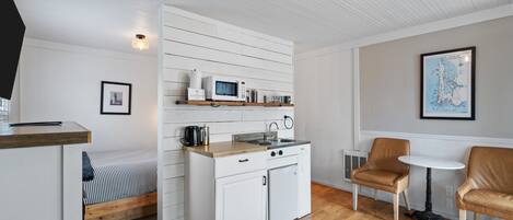A compact kitchen with a microwave, stove, and sink, a bed with striped bedding, and a small table with chairs.