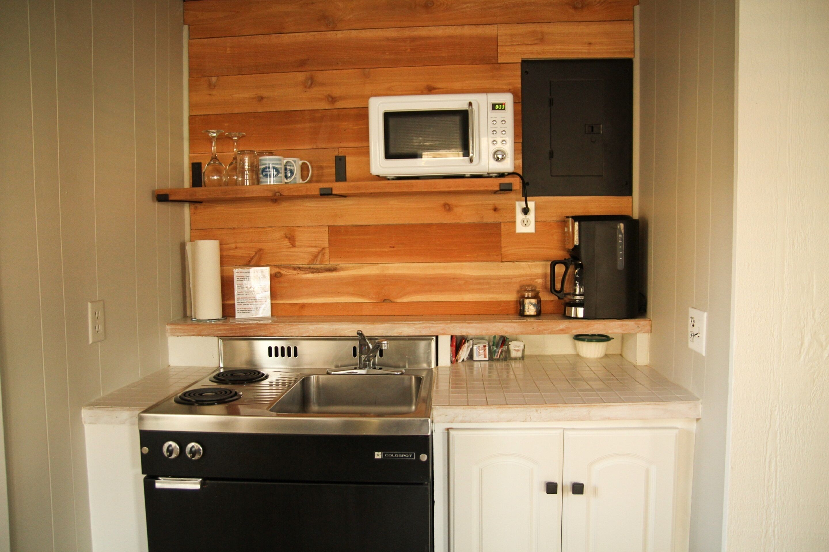 A compact kitchen with a stove, sink, microwave, and a coffee maker.