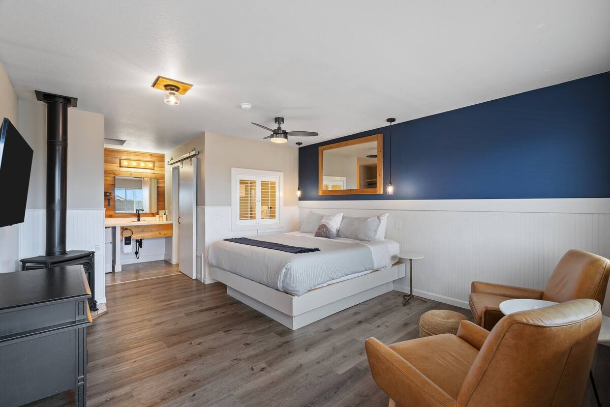 A modern bedroom with a large bed, a wooden floor, a ceiling fan, and a large mirror.