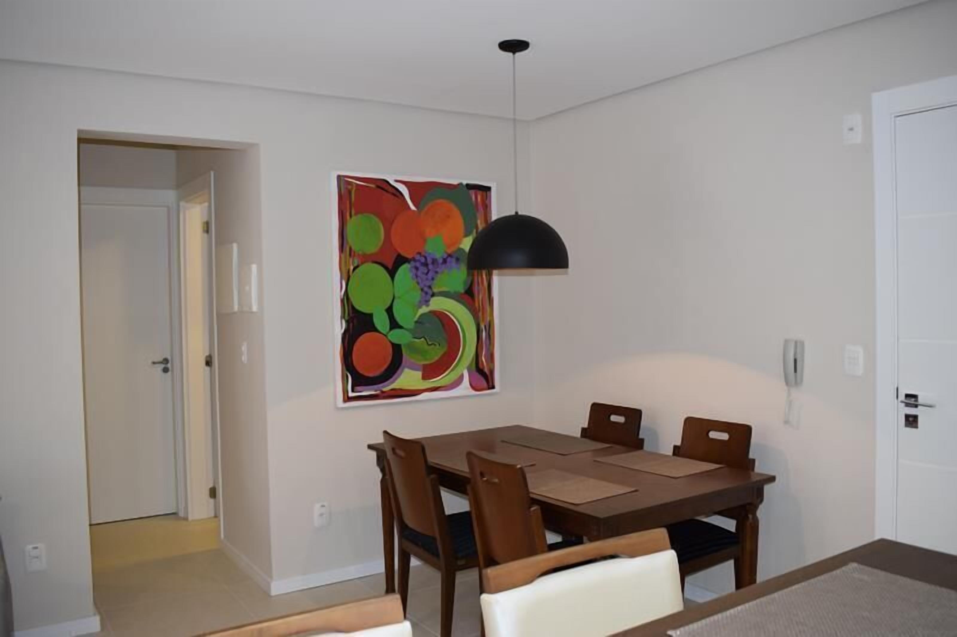 A dining area with a table and chairs, a colorful abstract painting on the wall, and a black pendant light.