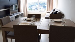 Un comedor con una mesa preparada para cuatro personas, un sofá y un televisor en la pared.