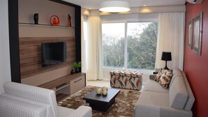 Una sala de estar moderna con un televisor de pantalla plana, un sofá, una mesa de centro con esferas decorativas y una ventana con cortinas.